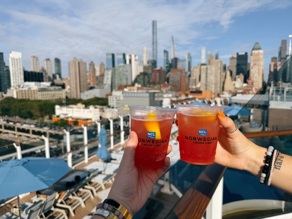 Two pink cocktails on a Norwegian ship with NYC skyline in the background. 